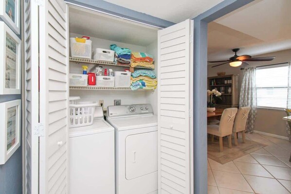 A laundry room with a washer and dryer, shelves with folded clothes, baskets, and storage bins.