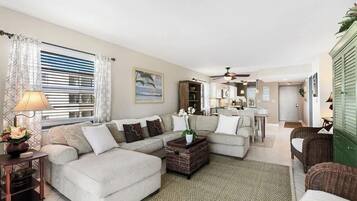 A spacious living room with a sectional sofa, a coffee table, and a dining area with wicker furniture.