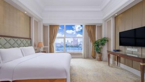 A hotel room with a bed, a TV, a window with a city view, and a plant. - Noble Hotel (Shanwei)