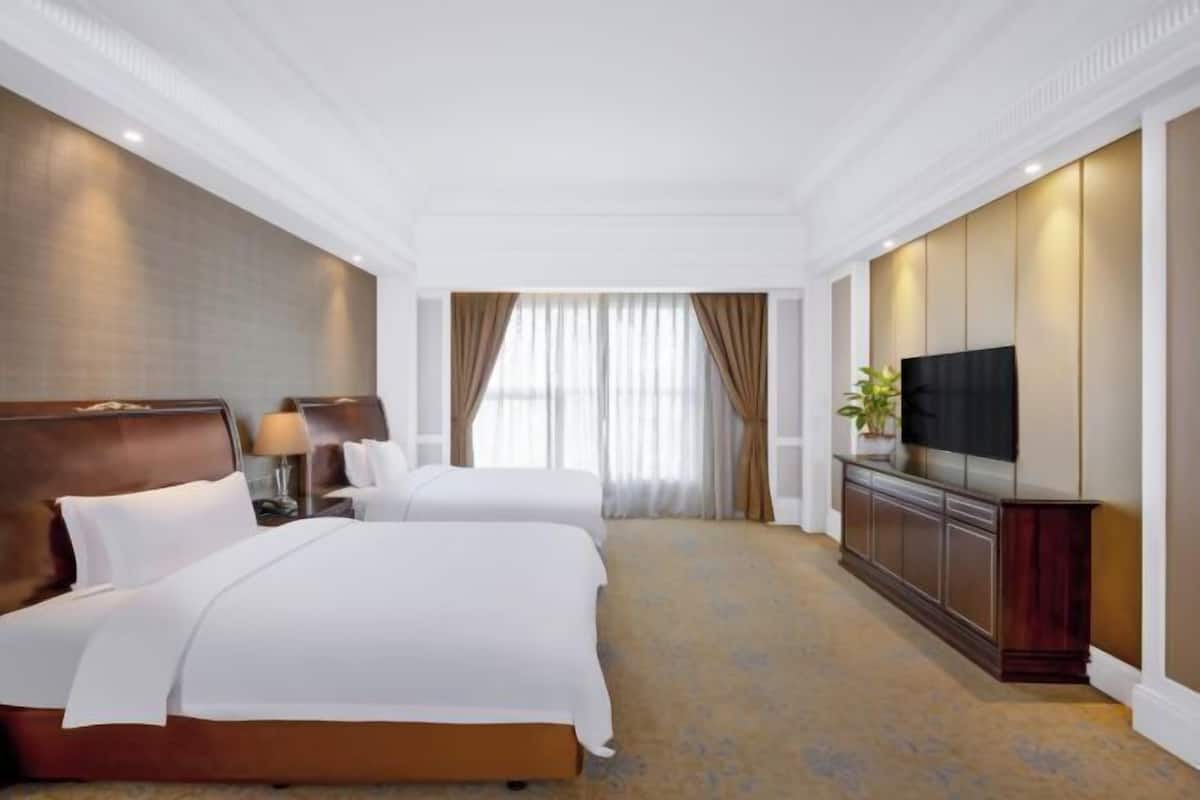 A hotel room with two beds, a TV, a nightstand, and a large window with curtains.