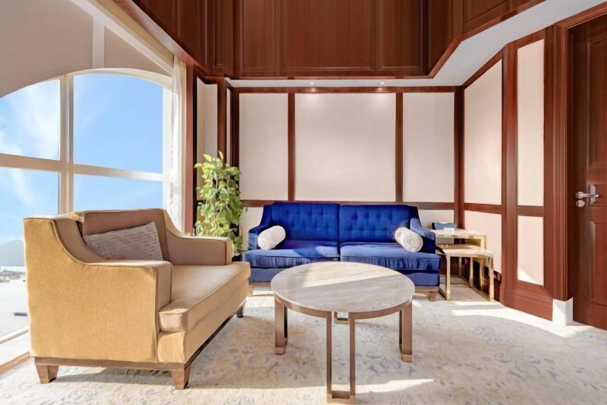 A room with a large window, a blue sofa, a beige armchair, and a round wooden table.