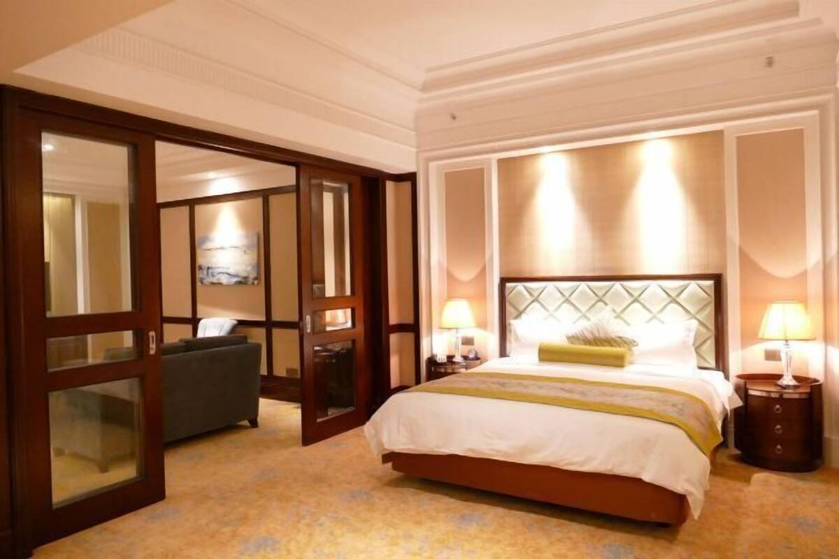 A hotel room with a large bed, two bedside tables with lamps, a sofa, and a large mirror.