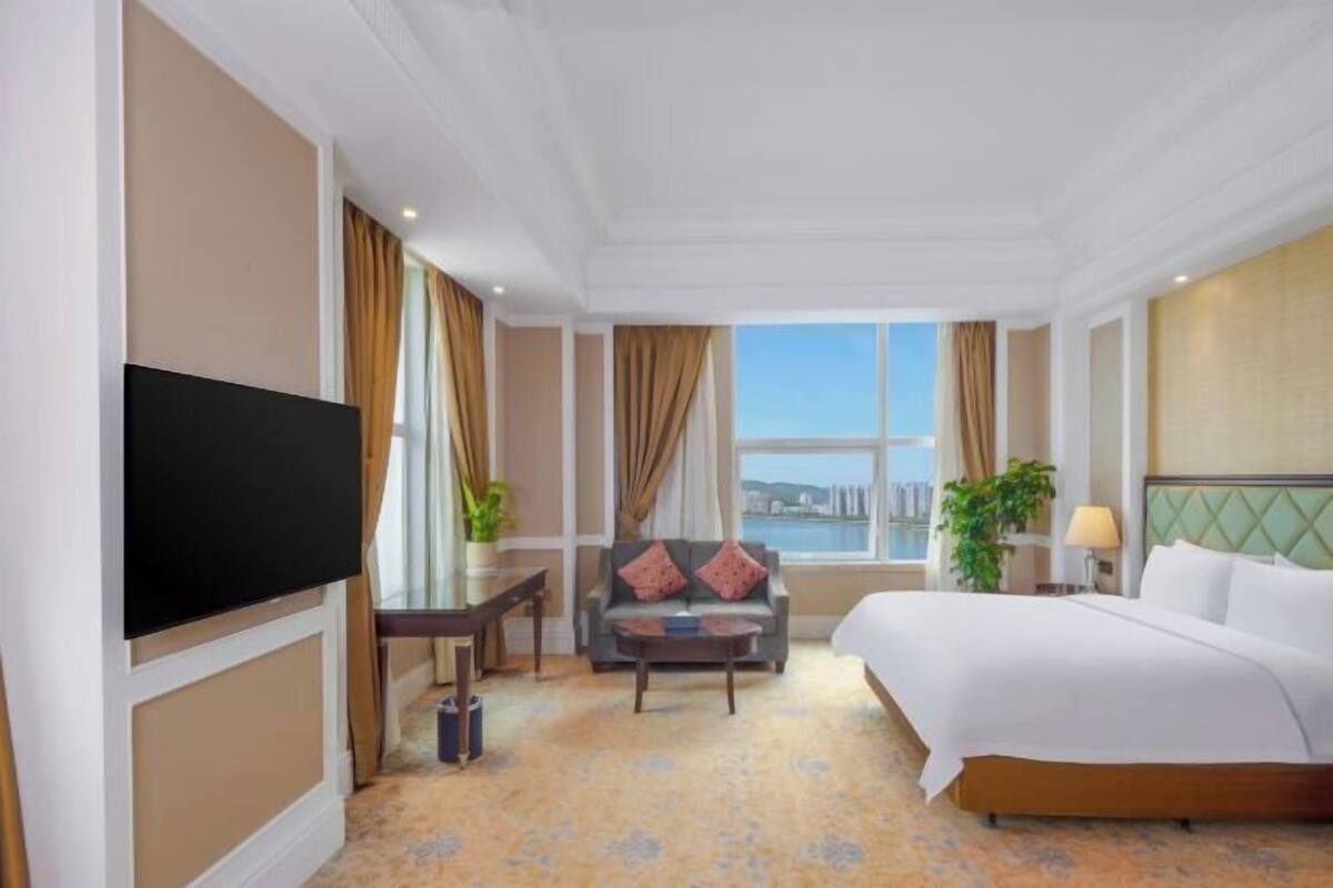 A hotel room with a bed, a television, a sofa, a coffee table, and a window with a view.
