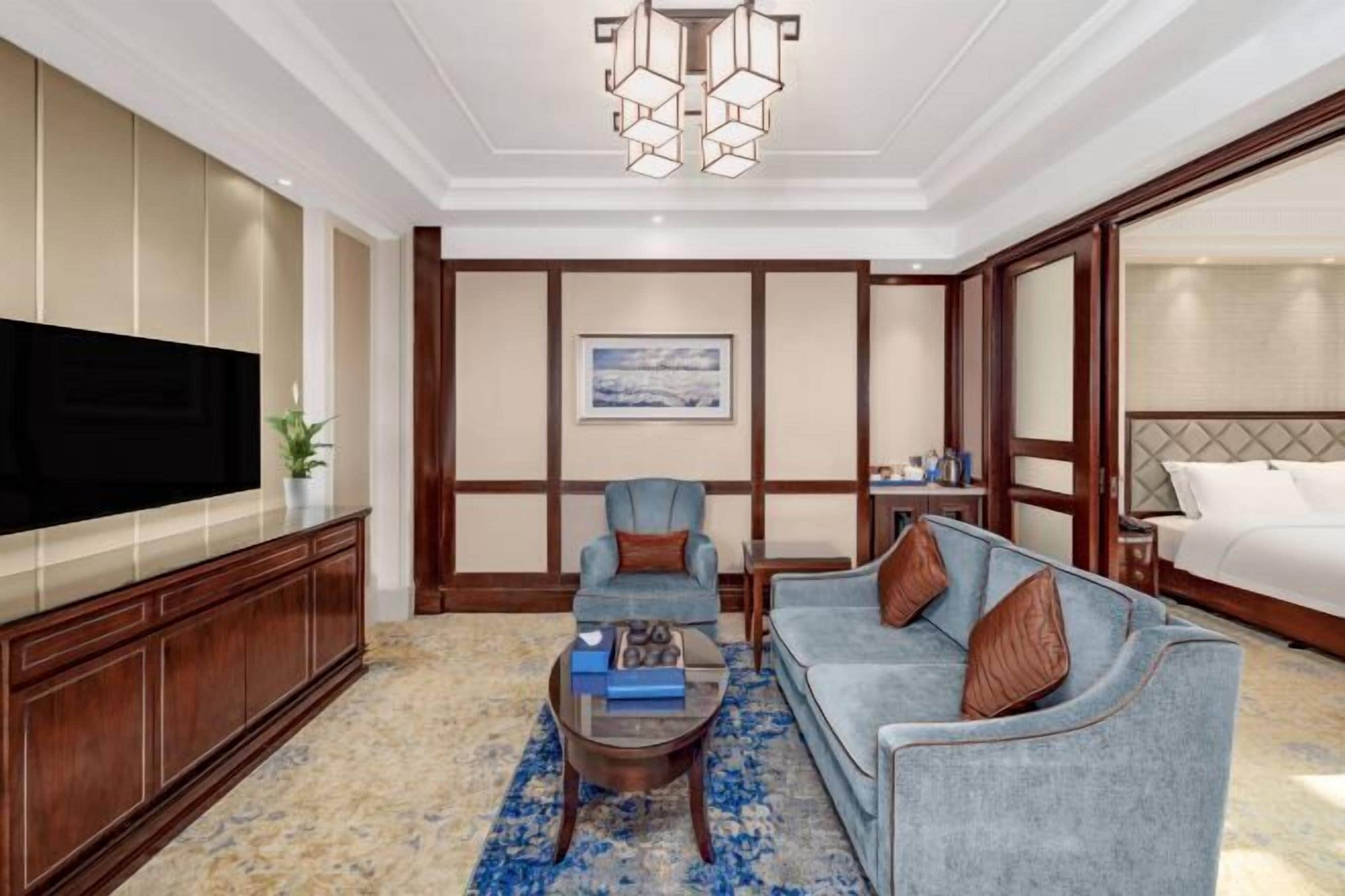 A hotel room with a large flat-screen TV, a sofa, a coffee table, and a bed.