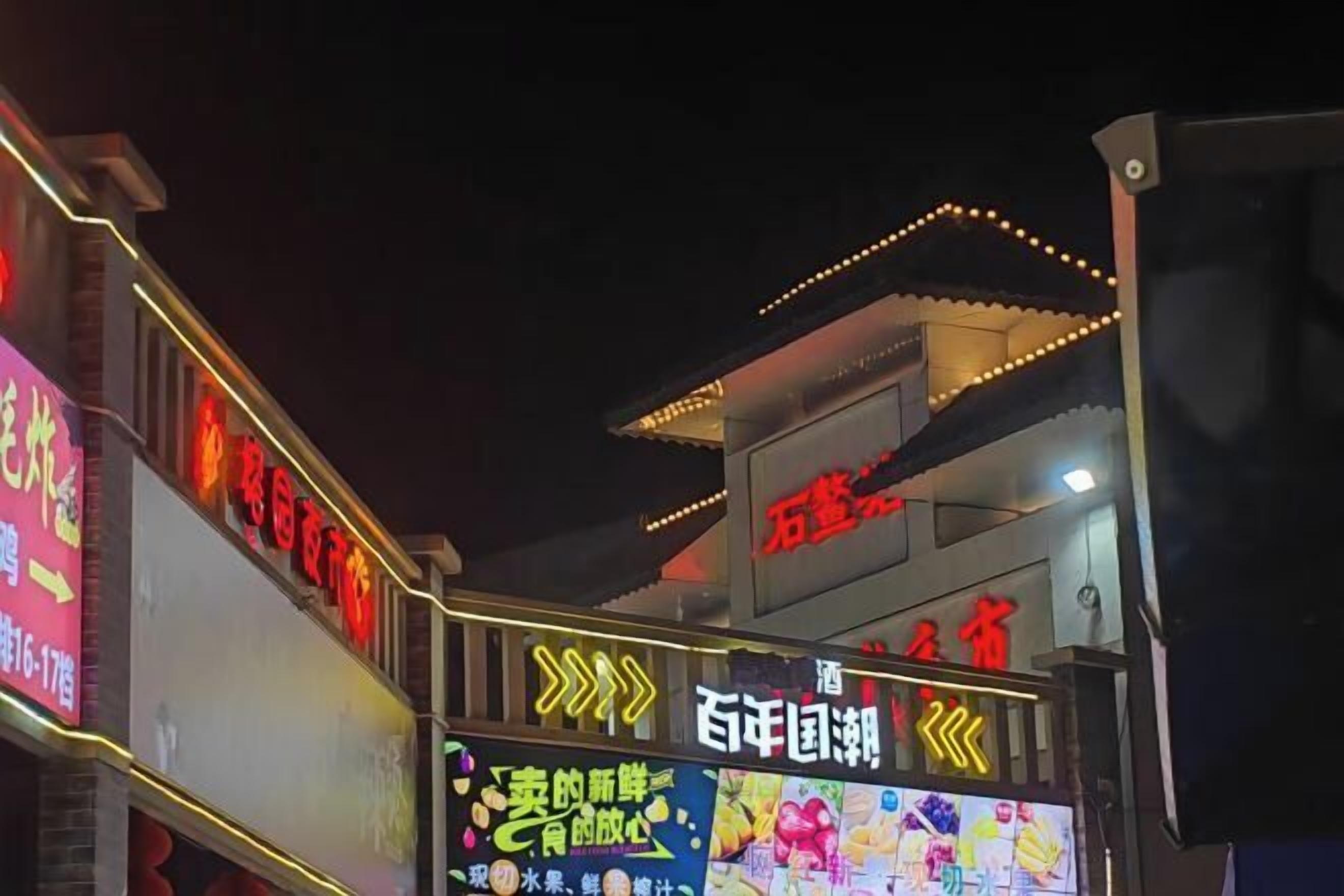 Un edificio con señalización iluminada, incluyendo un cartel rojo destacado y una flecha amarilla.