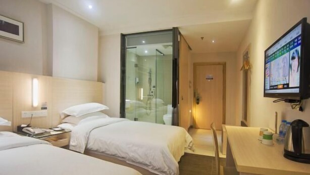 Habitación de hotel con dos camas, un escritorio, una silla, un televisor y una puerta de vidrio que da al baño.