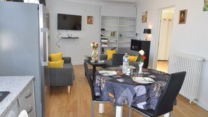 Ett kompakt bostadsutrymme med en matplats, ett litet kök och en TV som är monterad på väggen.