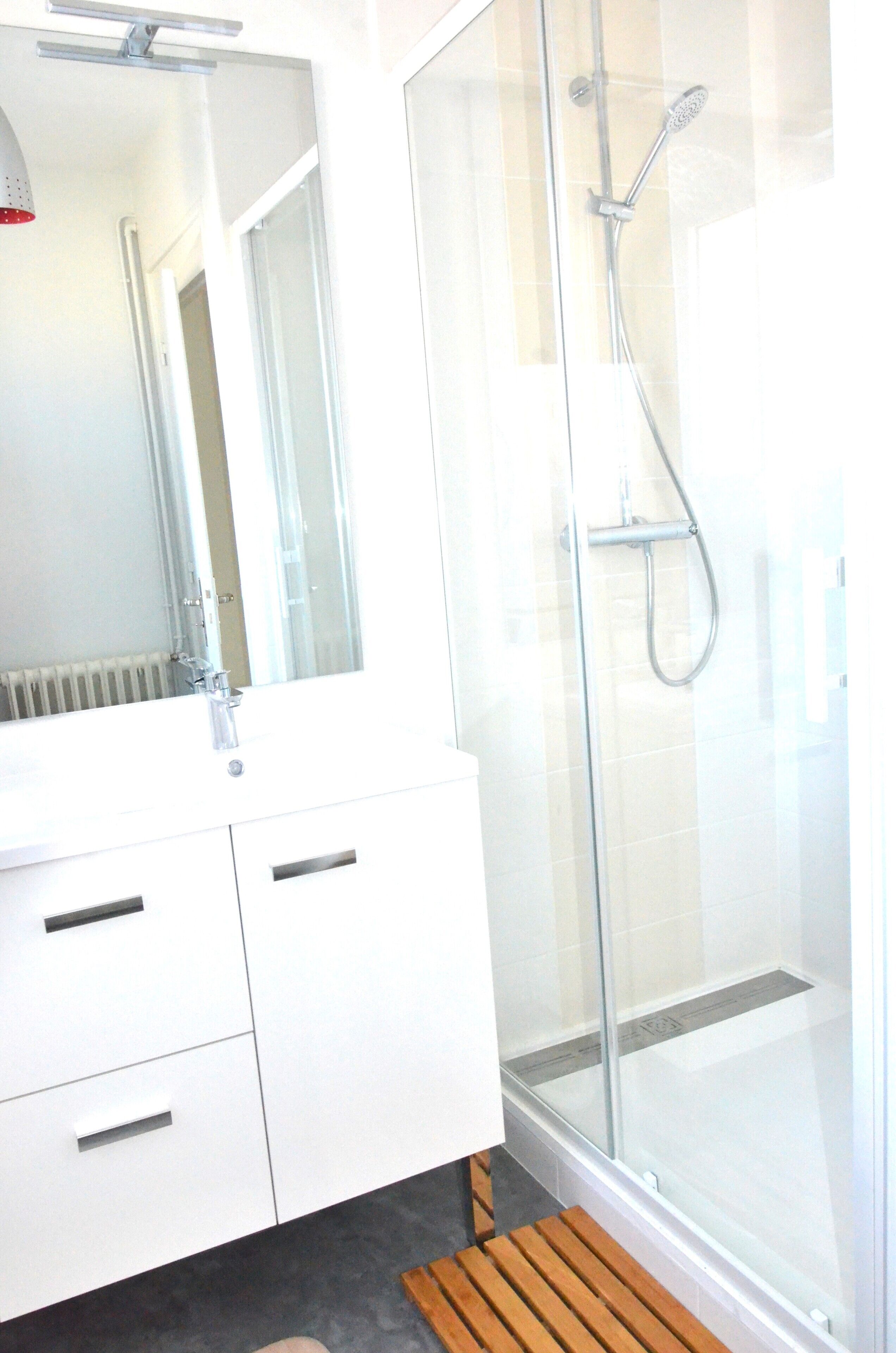 A modern bathroom with a glass shower enclosure, a white vanity with a mirror, and a wooden bench.