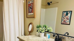 A bathroom with a white toilet, a sink with a granite countertop, a mirror, and a shower curtain.
