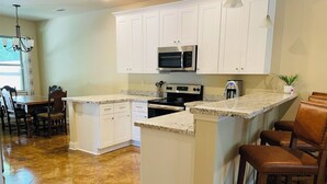 A kitchen with white cabinets, a granite countertop, a built-in microwave, a stove, and a dining area with wooden chairs and a table. - Beech St. fenced back yard, central location, garage (Covington)