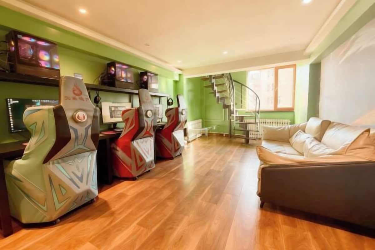 A modern living room with a sofa, gaming chairs, a staircase, and a TV on the wall.