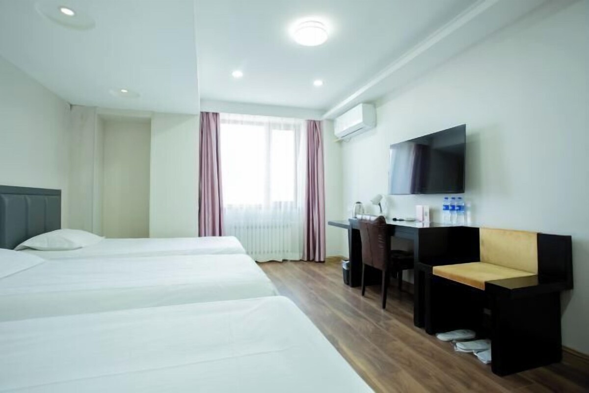 A hotel room with three beds, a desk, a chair, a TV, and a window with curtains.