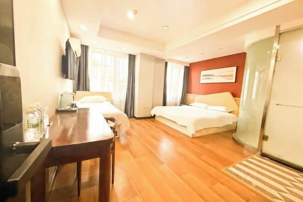 A hotel room with a wooden floor, a desk with a chair, two beds, a TV, and a glass door.