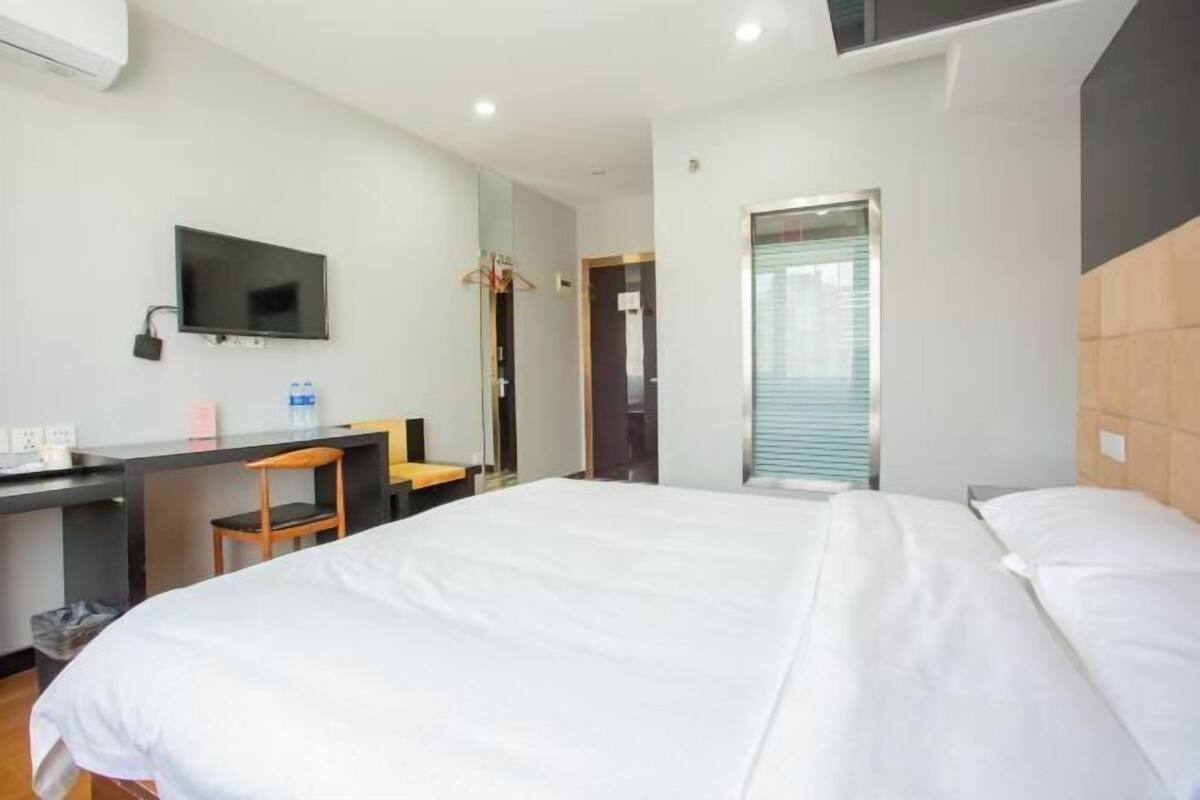 A hotel room with a bed, a desk, a chair, a television, and a door leading to another room.