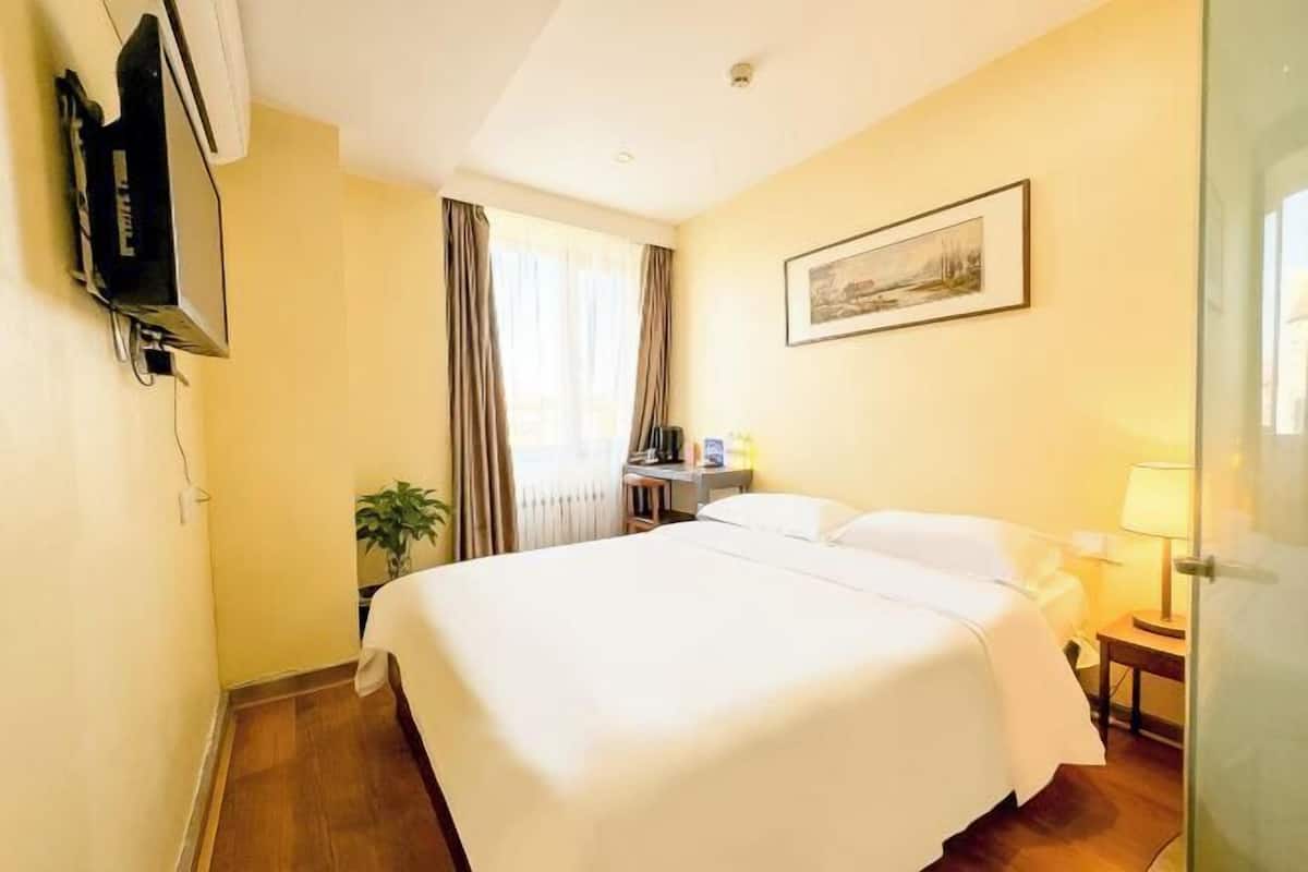 A hotel room with a large bed, a desk with a computer, a TV mounted on the wall, and a window with curtains.