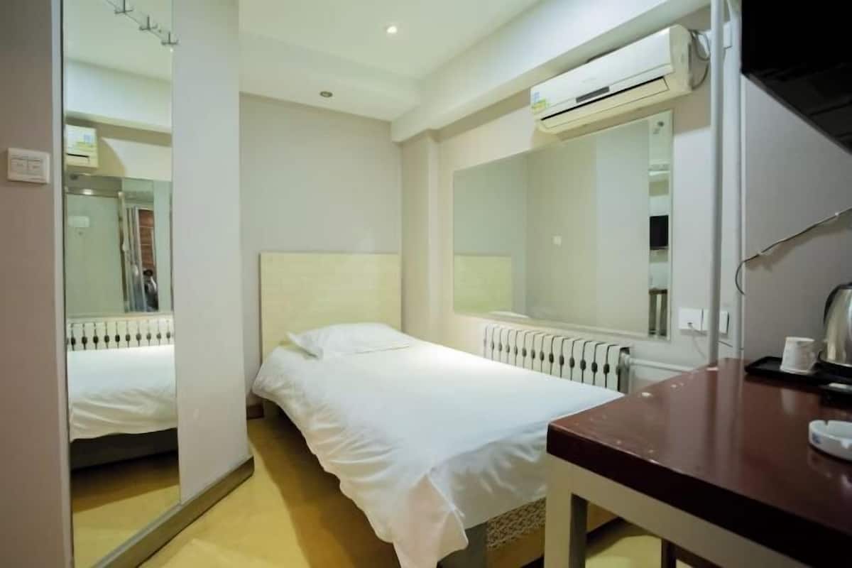 A hotel room with a bed, a desk, an air conditioning unit, a mirror, and a radiator.
