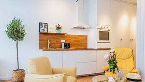 A modern kitchen with white cabinets, a wooden countertop, a built-in oven, and a yellow armchair.