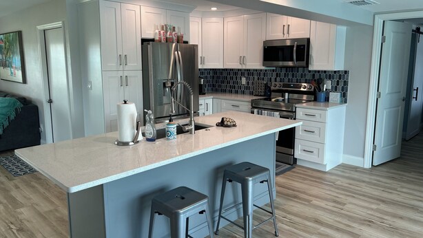 A modern kitchen with white cabinets, stainless steel appliances, and a central island with stools. - Relaxing 3 Br-2 Ba cottage on canal with heated pool & hot tub. (Cape Coral)