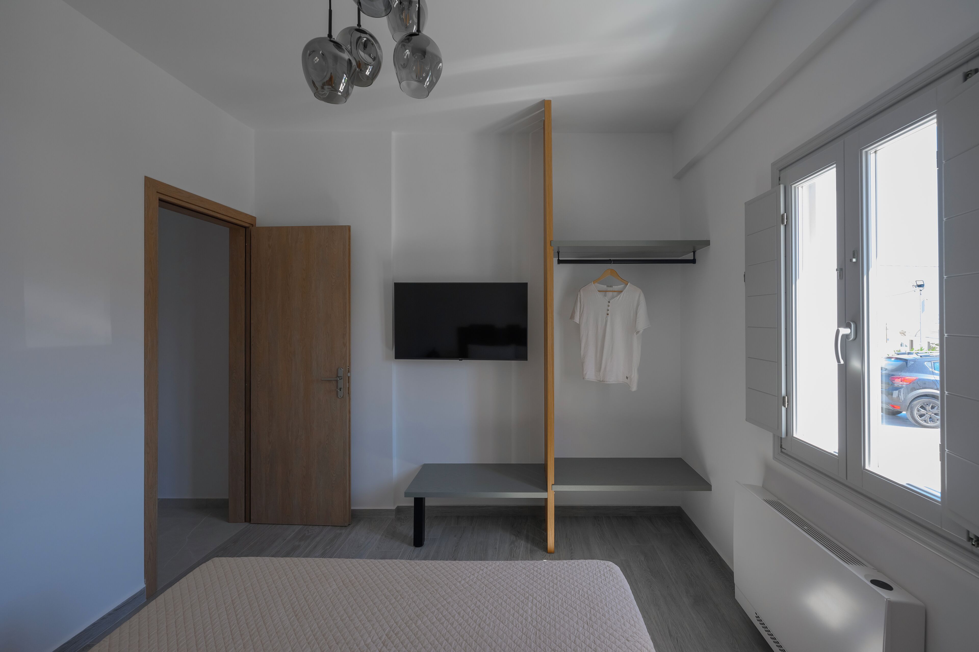 A modern bedroom with a bed, a bench, a TV, a wardrobe, and a window with a view of the outside.