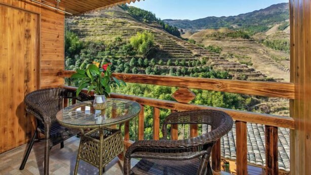 A wooden balcony with wicker furniture, a glass table, and a view of terraced fields. - Longji Rice Terraces Fengya Mountain Dwelling B&B (Longsheng)