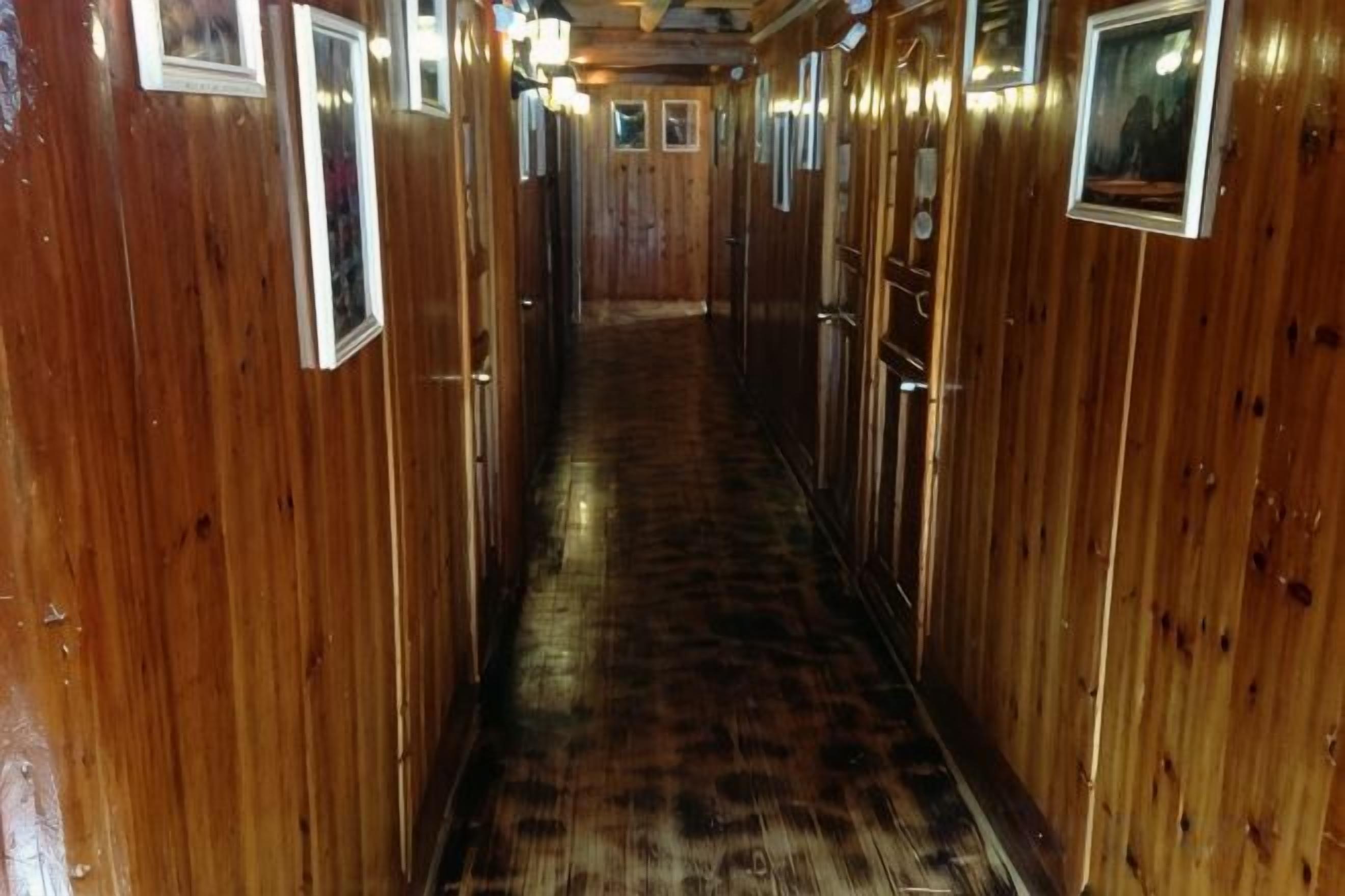 A narrow corridor with wooden walls and doors, leading to a central area.