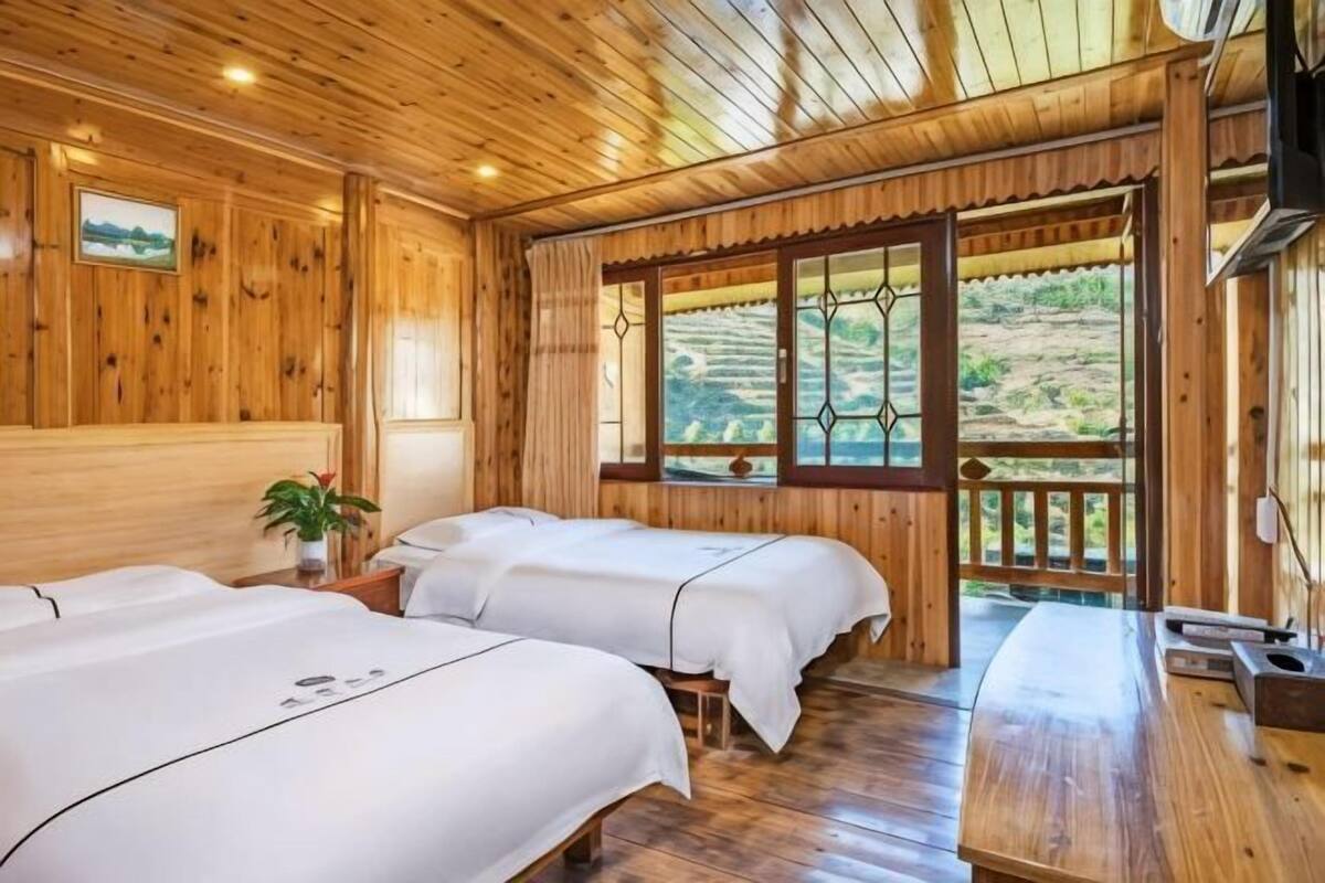 A wooden room with two beds, a wooden ceiling, and a window with a view of the countryside.