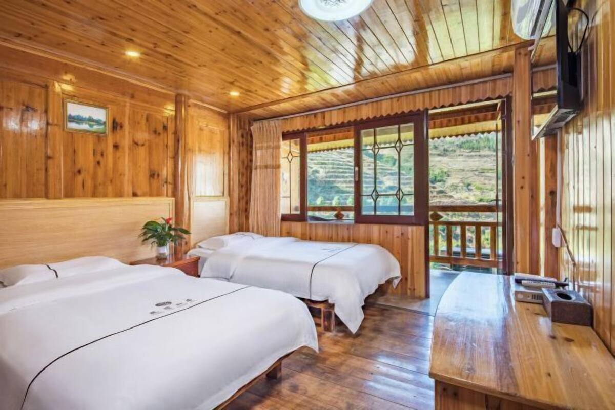 A wooden cabin with two beds, a wooden table, and a window with a view of a landscape.