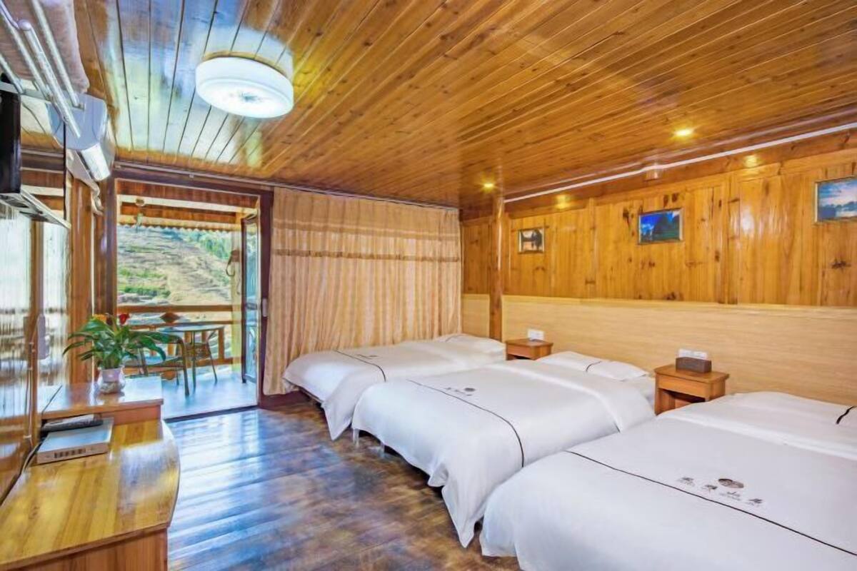 A wooden cabin with four beds, a dining area, and a large window overlooking a scenic landscape.