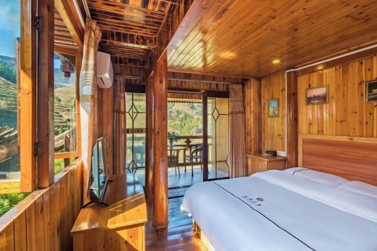 A wooden cabin with a bed, a TV, and a balcony with a view of the outdoors.