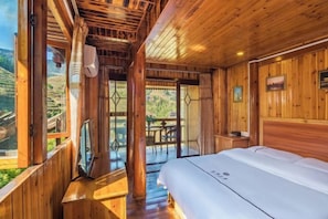 A wooden cabin with a bed, a TV, and a balcony with a view of the outdoors.