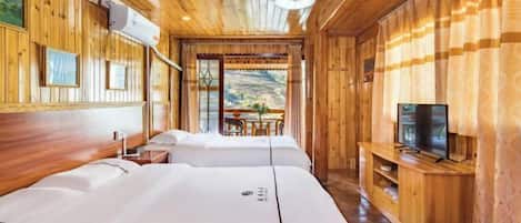 A wooden cabin room with two beds, a TV, and a dining area with a view of the outdoors.
