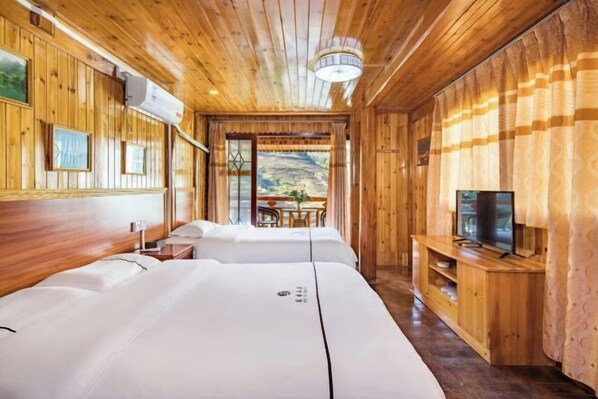 A wooden cabin room with two beds, a TV, and a dining area with a view of the outdoors.