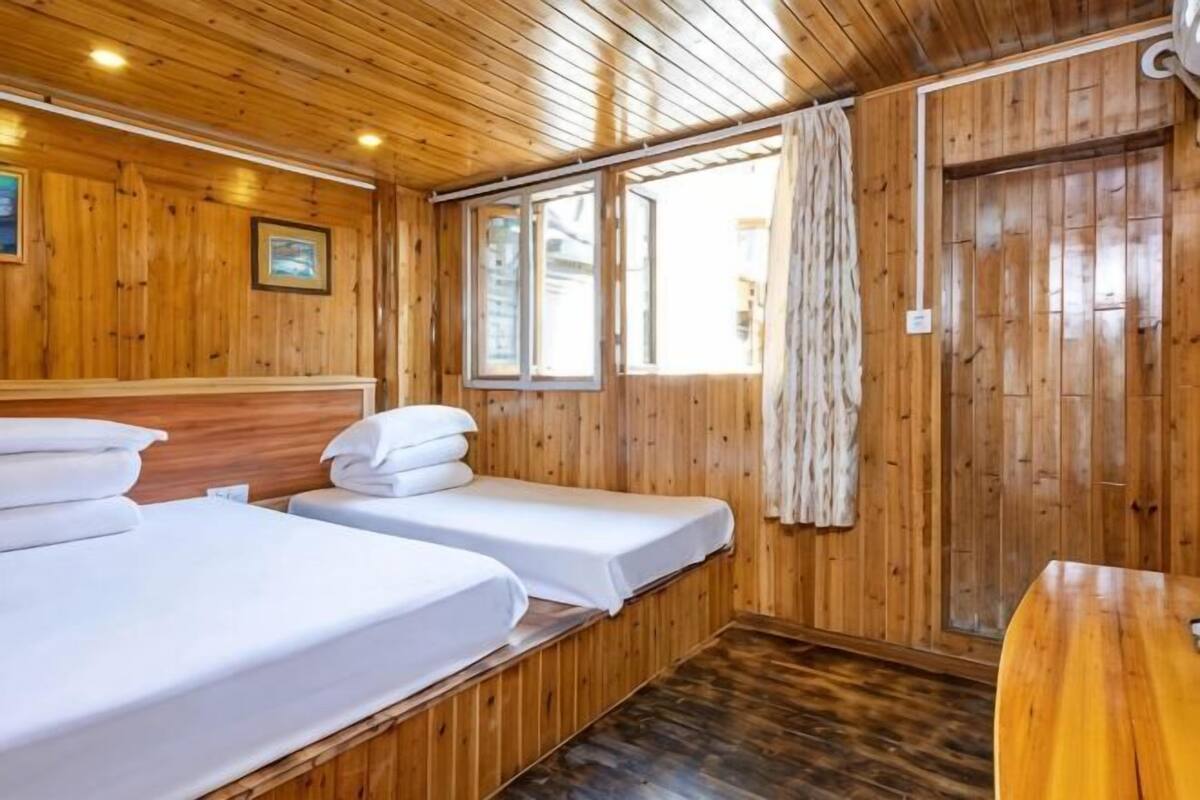 A wooden cabin room with two beds, a wooden table, and a window with curtains.