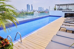 Ein Pool auf dem Dach mit Blick auf die Stadt, eine Holzterrasse und Liegestühle.