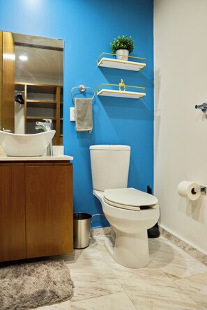 Ein modernes Badezimmer mit blauer Akzentwand, einem Holzwaschtisch, einer weißen Toilette und einem kleinen Mülleimer.