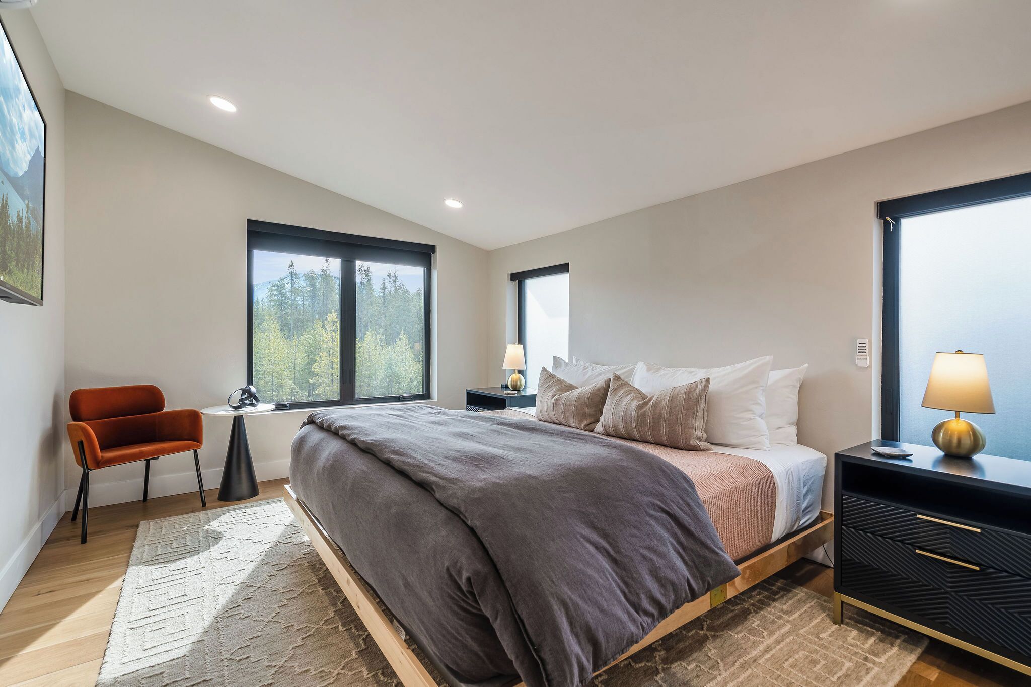 A modern bedroom with a bed, a chair, a desk, and a nightstand.