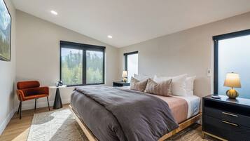 A modern bedroom with a bed, a chair, a desk, and a nightstand.