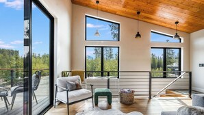 Habitación amplia con ventanas grandes, techo de madera y vista a un bosque.