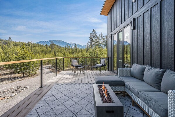 A modern outdoor deck with a sofa, chairs, and a fire pit. - Minutes from Glacier National Park’s west entrance (West Glacier)