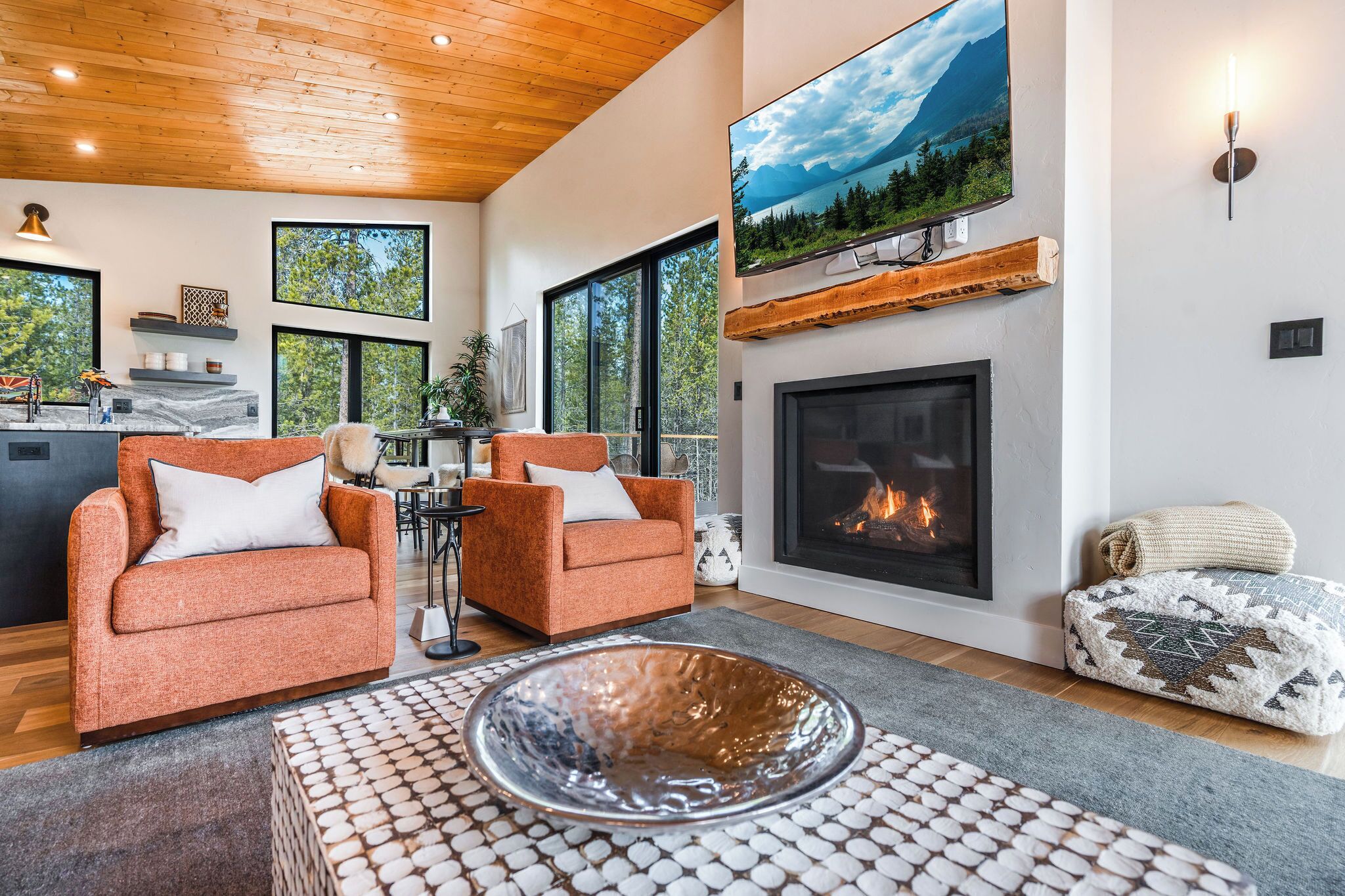 A modern living room with two orange armchairs, a fireplace, a large TV, and a wooden ceiling.