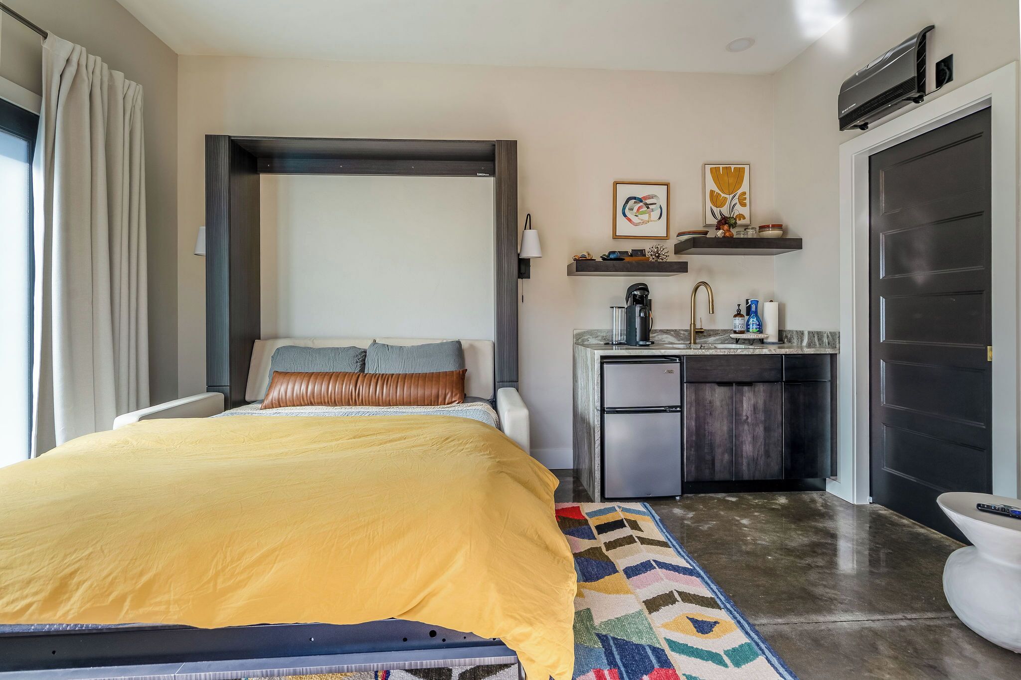 Une chambre d’hôtel moderne comprenant un lit, une petite kitchenette, une salle de bain et une vue sur l’extérieur.