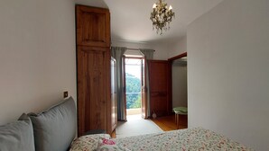 A bedroom with a bed, wooden wardrobe, and a view through an open door to a balcony.