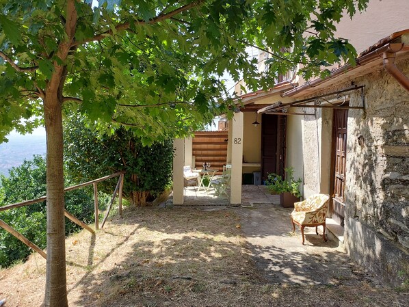 Un espacio al aire libre rústico con pared de piedra, pérgola de madera y vistas a una colina.