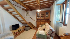 A cozy living room with a wooden staircase, a floral sofa, a wooden cabinet with glass doors, and a television on a wooden stand.