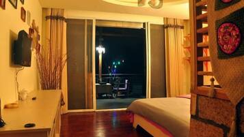 A bedroom with a bed, a desk, a chair, a TV, and a balcony with a table and chairs.