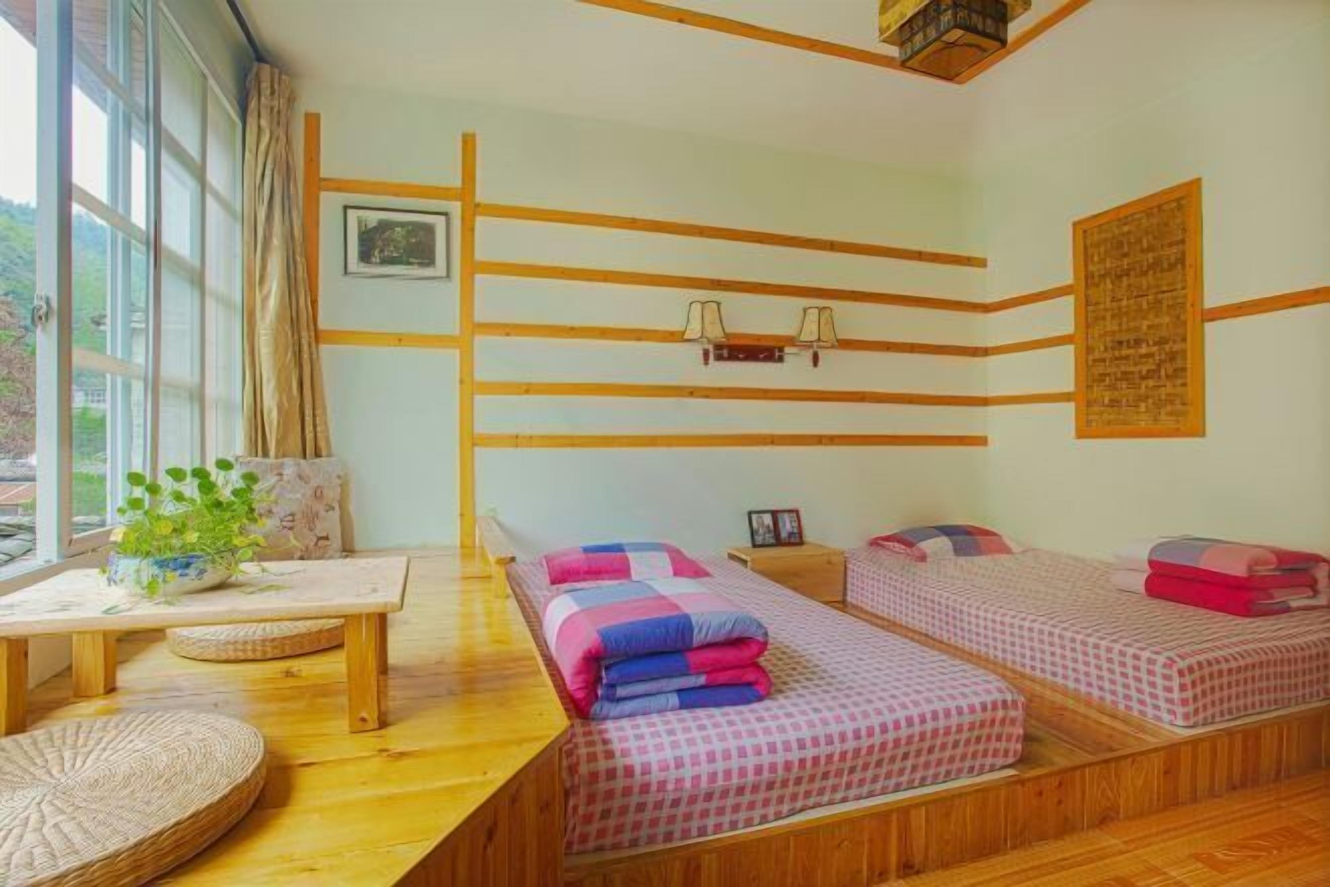Een kamer met twee bedden, een houten tafel, een raam met gordijnen en een wandlamp.