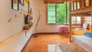 Una habitación con literas, una mesita, una silla, un televisor y cuadros en la pared.