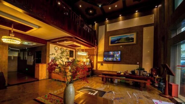 A lobby with a wooden reception desk, a vase with flowers, a television screen, and a large window. - Boao Yingke Hotel (Dali City)