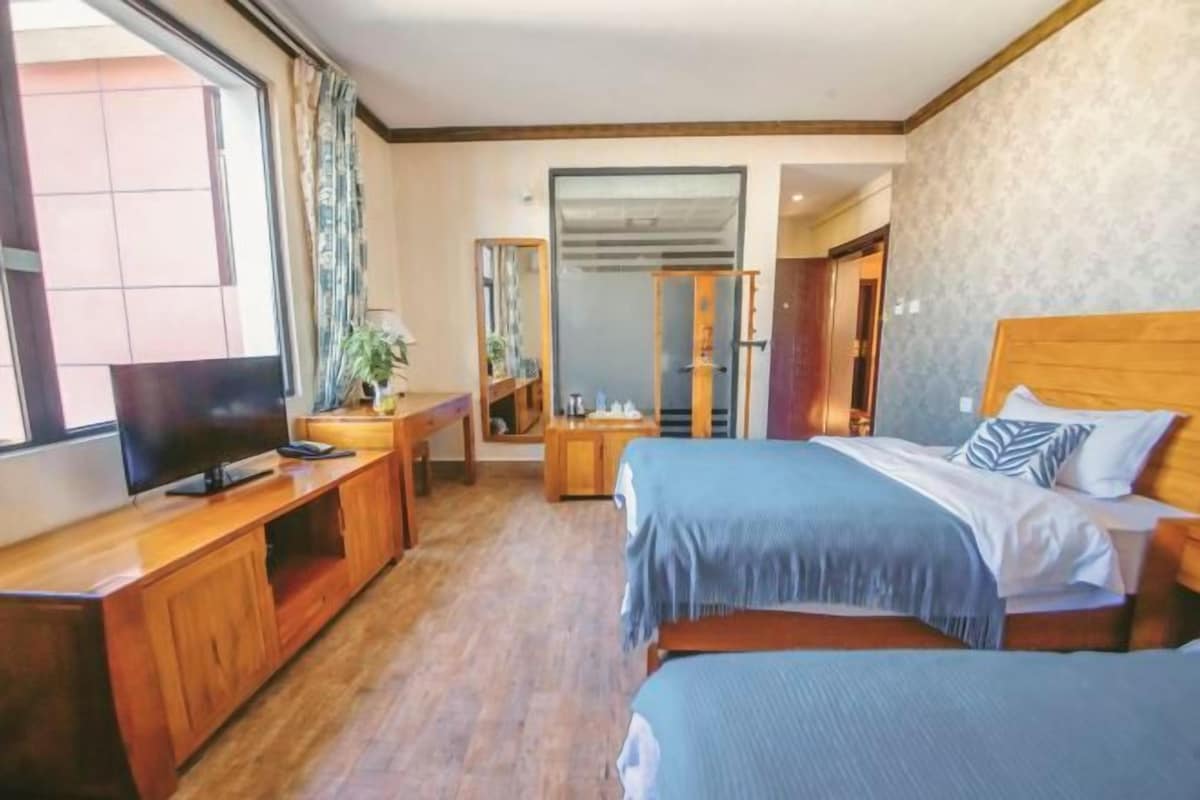 A hotel room with two beds, a TV, a desk, and a mirror.