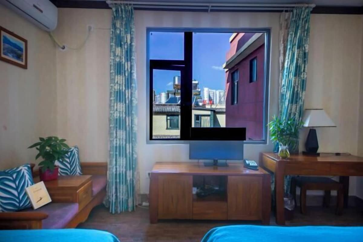 A room with a large window, a television, a sofa, a small table, and a desk.